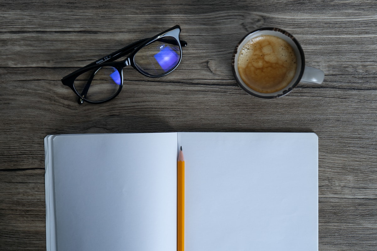An open notebook and warm drink on a table.