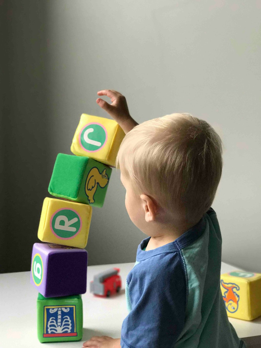 A young child reaching for a tall stack of wooden letter blocks.